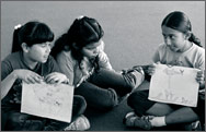 Three girls sitting and showing their drawings